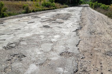 Kötü yol, asfalt çatlamış çukurlar ve büyük delikler. Yoldaki çukurlar ve asfaltta taşlar. Asfalt yüzeyi yolda yok oldu. Yolun kötü durumda, onarılması gerekiyor..