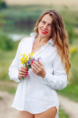 Güneşin tadını çıkaran, elinde bir buket kır çiçeği tutan nazik, güzel genç bir kadın. Bir buket kır çiçeğiyle çekici bir kız. Yumuşak yaz fotoğrafı.