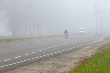 Siste arabalar ve scooter var. Kötü kış havası ve yoldaki tehlikeli trafik. Sisli bir günde hafif araçlar. Kötü yağmurlu havalarda kazaların tehlikesi hakkında sezonluk uyarı.