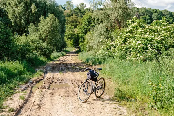 A touring bicycle stands in the middle of a dirt road with puddles and mud in the countryside.