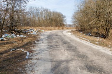 Yolun kenarında bir çöplük var. Yolun kenarına bırakılmış plastik atık yığınlarının manzarası tarlaların ağaçlarının yanında..