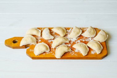 Ahşap bir tahtanın üstünde el yapımı bir Varenyky. Tahtada hamur köftesi pişirmek. Çiğ vareniki ve süzme peynir.