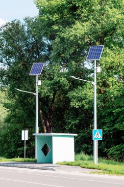 Mavi gökyüzü ve ağaçlarla kaplı yol üzerinde güneş paneli olan lamba direği. Güneş panelleri kullanarak otonom sokak ışıklandırması. Sokak lambası, güneşten gelen pillerle. Alternatif yenilenebilir enerji sistemleri.