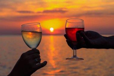 A man and a woman clink champagne glasses against a dramatic sunset sky. Wine glasses at sunset on the beach. Selective focus. Silhouette of two hands with a glass of wine. clipart