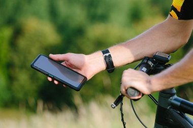 Bisikletçi doğada bir bisikletin arka planında beyaz ekran akıllı telefon modeli tutuyor. Akıllı telefonlu yakın plan el..