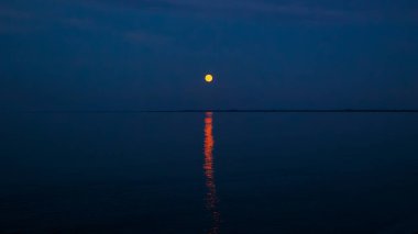 Gece denizde dolunay var. Ukrayna Karadeniz manzarası. Dolunay, okyanusun üzerinde gece gökyüzünü aydınlatır. Suya güzel bir parıltı yayar ve dingin bir atmosfer yaratır..