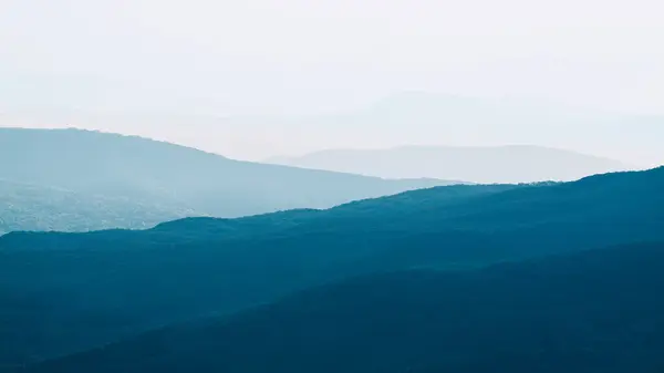 Görünür siluetlerle sabah sisli dağlarda. Gün batımında dağlarda sakin bir akşam manzarası. Resim duvar kağıtları. Doğal arka plan. Panorama. Kırım, Ukrayna.