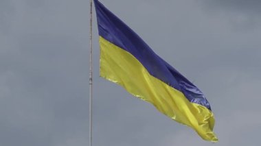 Hasarlı bir Ukrayna bayrağı bulutlu bir gökyüzünün arka planında dalgalanıyor. Ukrayna bayrağı bulutlu bir gökyüzüne karşı metal bir direkte