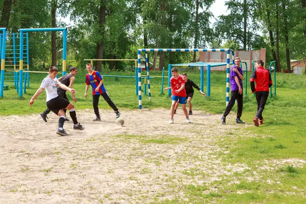 16 Mayıs 2023, Romny, Ukrayna: Gençler yeşilliğin ortasında bir yaz spor sahasının çimlerinde sokak futbolu oynuyorlar. Yüzlerde canlı duygular ve oyunda top