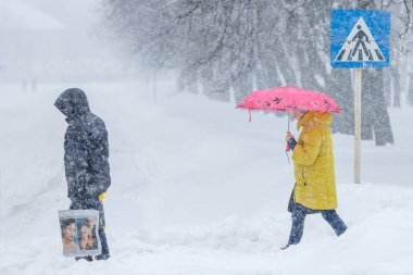 Ukrayna, Romny şehri, 08.01.2016: Yoğun bir kar yağışı sırasında karlı bir şehir caddesi. Yaya geçidi. Kaldırımlarda, arabalarda ve ağaç dallarında çok kar var. İnsanlar karşıdan karşıya geçiyor. Soğuk karlı hava.