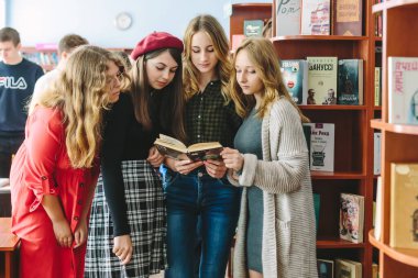 Romny, Ukraine, September 29, 2019: Young women, students are standing in a cozy library environment and reading a book clipart