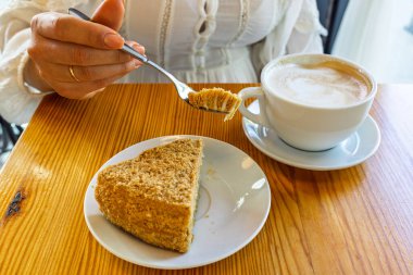 Sıcak bir kafede bir fincan kahveyle bir parça kekin tadını çıkaran bir adamın yakın çekimi. Tahta bir masa ve lezzetli bir tatlı rahatlatıcı bir atmosfer yaratır..