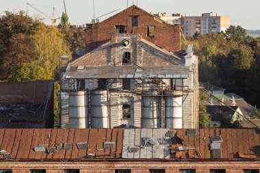 An old abandoned industrial building with a rusty roof and sheets of corrugated iron strewn across the roof after a storm, emphasizing its dilapidated state. clipart