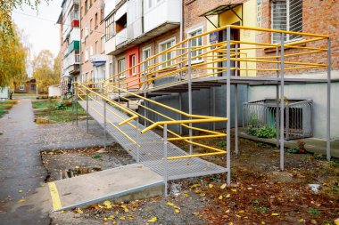 Parlak sarı korkuluklu yeni yapılmış bir rampa tuğla bina girişine çıkıyor. Eve yakın engelliler için bir rampa..