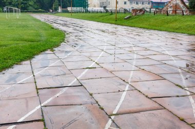 Stadyumdaki eski hasarlı koşu pistinde soluk beyaz çizgiler ve yeşil çimenler ve tarlalarla çevrili kırık fayanslar. Kentsel spor tesisleri kavramı.