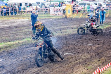 Ukrayna, Romny, 2-3 Haziran 2018: Arka planda seyirciler ve etkinlik personeli ile ıslak ve çimenli bir pistte yarışan genç yarışçılarla Ukrayna Motocross Şampiyonası.