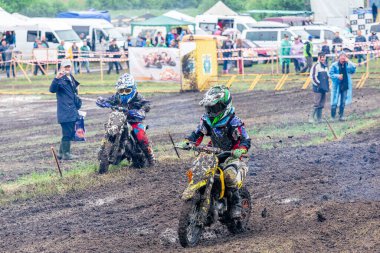 Ukrayna, Romny, 2-3 Haziran 2018: Arka planda seyirciler ve etkinlik personeli ile ıslak ve çimenli bir pistte yarışan genç yarışçılarla Ukrayna Motocross Şampiyonası.