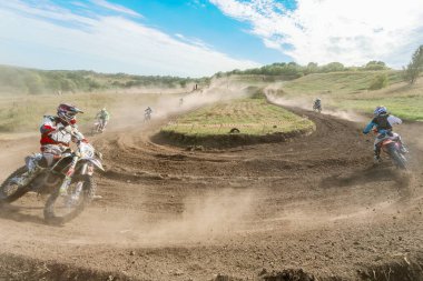 Ukrayna, Romny, 5-6 Eylül 2020: Dar virajlarda ve engebeli arazide hareket eden motorcularla dinamik motokros yarışı, açık arazi ve parlak gökyüzü altında toz bulutları.