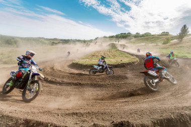 Ukrayna, Romny, 5-6 Eylül 2020: Dar virajlarda ve engebeli arazide hareket eden motorcularla dinamik motokros yarışı, açık arazi ve parlak gökyüzü altında toz bulutları.