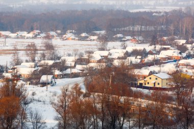 Kış manzarasının arka planında evleri ve ağaçları olan karlı bir köy. Köyün kuş bakışı görüntüsü. Kış mevsimi ve kırsal yaşam kavramı.