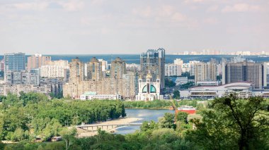 Konut binaları, yemyeşil yemyeşil ve bulutlu gökyüzünün altındaki nehir manzaralı Kyiv şehrinin panoramik manzarası. Şehir manzarasının hava fotoğrafçılığı. Kentsel gelişim ve doğa kavramı