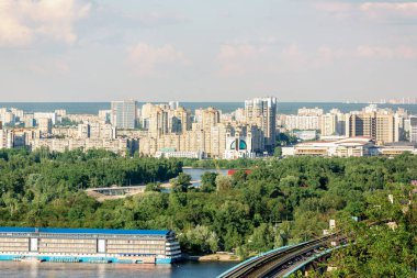Konut binaları, yemyeşil yemyeşil ve bulutlu gökyüzünün altındaki nehir manzaralı Kyiv şehrinin panoramik manzarası. Şehir manzarasının hava fotoğrafçılığı. Kentsel gelişim ve doğa kavramı