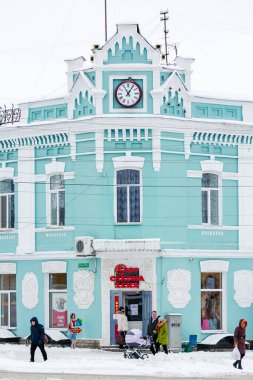 January 31, 2021 Romny, Ukraine: A beautifully decorated historic turquoise building with a clock tower covered with snow, with pedestrians passing a winter day. clipart