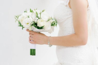 Beyaz dantelli gelinlik içinde bir gelin elinde bir buket taze beyaz gül ve lisianthus, aşkı ve saflığı simgeliyor..