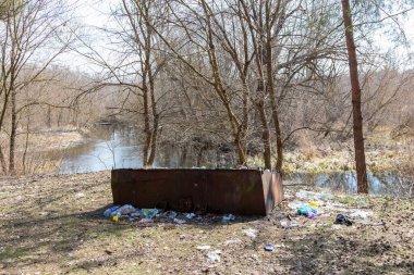 Ukrayna, Romny, 7 Nisan 2021: Etrafı plastik şişeler ve çöplerle çevrili taşmış bir metal çöp kutusu, çevre kirliliğini vurguluyor.
