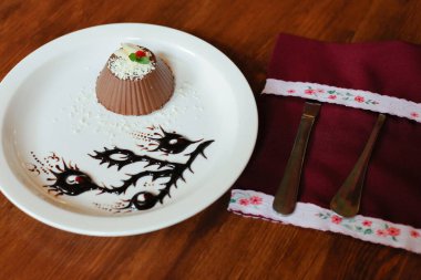 Elegant chocolate dessert garnished with white chocolate shavings, fruit, and mint, served on a plate with artistic chocolate sauce design. clipart