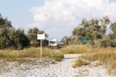 Bir kervan kumlu bir sahile yakın park etmiş, etrafı vahşi bitki örtüsü ve ağaçlarla çevrili, huzurlu ve tenha bir kamp yeri yaratıyor..