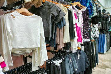 Bir perakende mağazasında askılarda sergilenen gömlekler, etekler ve ceketler de dahil olmak üzere çeşitli modaya uygun giyim ürünleri.