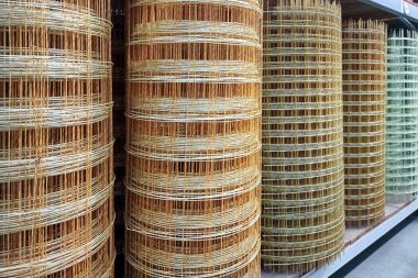 Bir mağazada, eskrim için kullanılan doğal malzemelerin altını çizerek çeşitli gölgelerde örülmüş dikey rattan rulo yığınları sergileniyor. Dokular ve desenler görsel ilgi yaratıyor