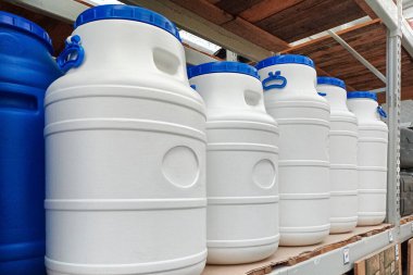 Beyaz ve mavi plastik fıçılar sanayi ve yerli kullanım için uygun bir şekilde depolama raflarında düzgün bir şekilde düzenlenmiştir. Her varilde mavi bir başlık ve kabzası var.