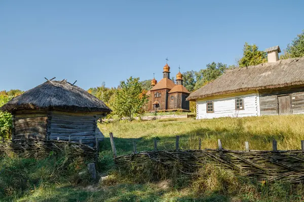 Sazdan çatılı evlerin, altın kubbeli ahşap bir kilisenin ve açık mavi gökyüzünün altında örülmüş bir çitin olduğu bir köy manzarası..