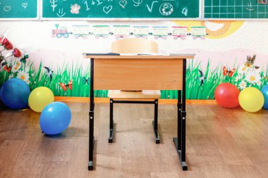 Tek kişilik öğrenci masası, balonlar, matematik temalı karatahta ve küçük çocuklar için eğlenceli duvar süslemeleri olan parlak ve neşeli bir sınıf..