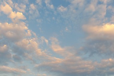 Sıcak günbatımı ışığı ile aydınlanan bulutlar sakin mavi gökyüzünde yumuşak ve sakin bir akşam atmosferi yaratıyor..