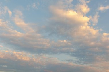 Sıcak pastel bulutlar, altın saatinde sakin bir akşam gökyüzünde süzülür. Mükemmel bir doğal arka plan ya da hava durumu sunar.