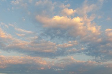 Yumuşak pastel bulutlar, gün batımında sakin mavi bir gökyüzünde süzülür, yukarıda huzurlu ve rüya gibi bir atmosfer yaratır.