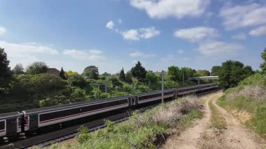 Güneye giden bir LNER InterCity 225 treni, Leeds 'ten Londra' ya giden bir trenle Sandy 'den geçer. Kuzeye giden 9 vagonluk Hitachi AT300 Azuma trenini geçer..
