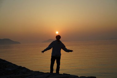 Asyalı bir adamın silueti. Güzel bir gündoğumu ve deniz altyapısı var.