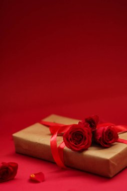 Kırmızı arka planda kırmızı kurdele ve güllerle sarılı bir hediye. Anneler Günü için sevgi ve özenin mükemmel bir sembolü..