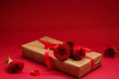 Kırmızı arka planda kırmızı kurdele ve güllerle sarılı bir hediye. Anneler Günü için sevgi ve özenin mükemmel bir sembolü..