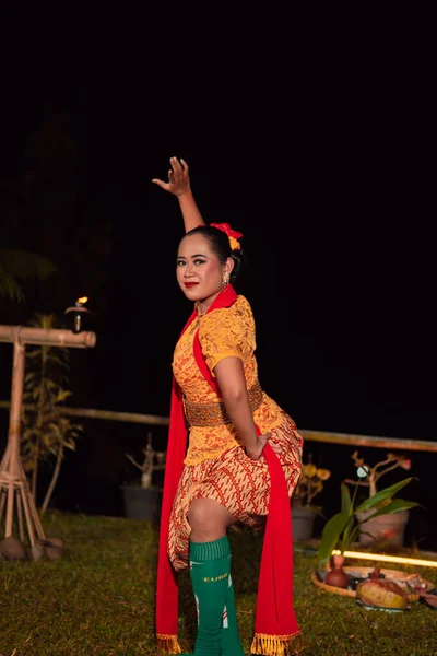 Asian woman performing a traditional dance called jaipong in Indonesia with a yellow dress and red scarf at the dance festival