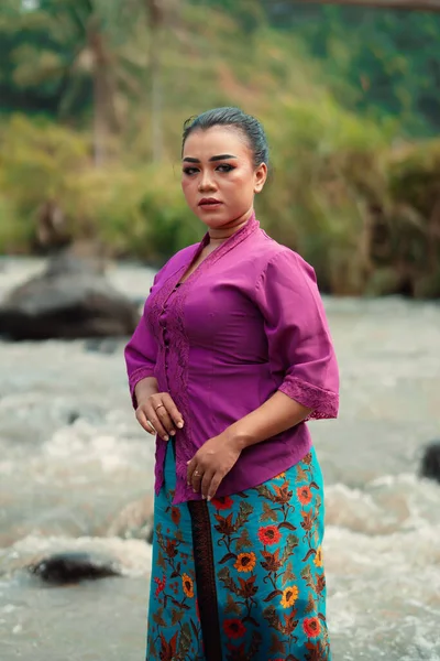 川の前に立つアジアの女性は 村の中を背景に美しい化粧と川の紫のドレスを着ている — ストック写真