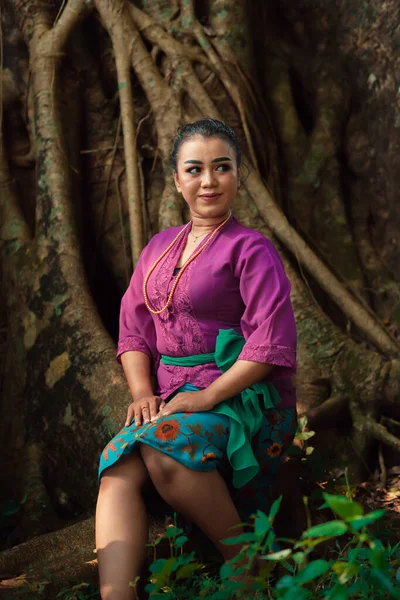 一位亚洲女人穿着紫色衣服 美丽地坐在大树上 在日光下游览丛林 — 图库照片