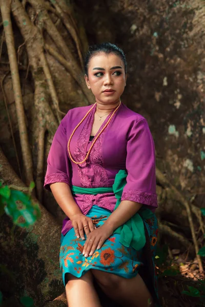 昼間にジャングルを訪れながら紫のドレスを着た大きな木の上に美しく座っているアジアの女性 — ストック写真