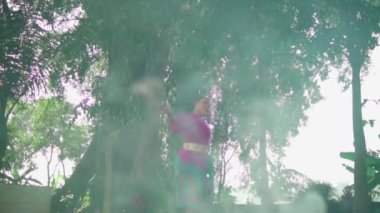 Yanan çöpün dumanının yanında dans eden Asyalı bir kadın öğleden sonra ormanda geleneksel pembe bir elbise giyerken.