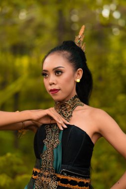 Portrait of a mystical woman in makeup with black hair and wearing a gold jewelry in front of the forest