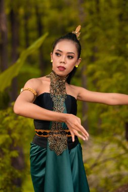 Javanese woman dancing in front of the woods in green costume while in makeup and performing at the village